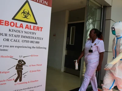 Health workers in protective gear beside an Ebola alert notice
